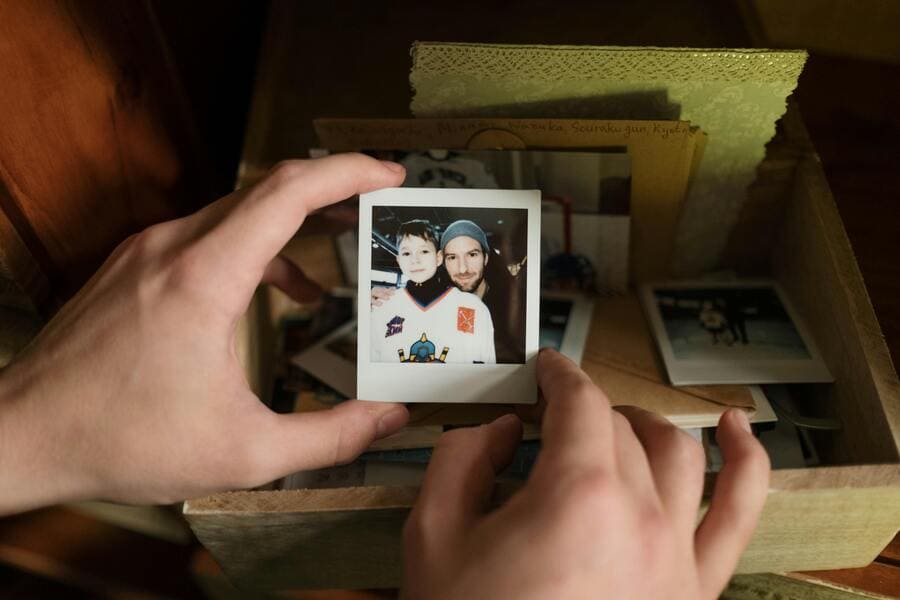 Manos sosteniendo una foto polaroid mientras crean una caja de recuerdos con pertenencias de un difunto.