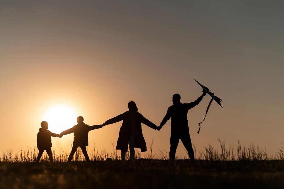 Familia disfrutando de un día al aire libre con un papá volando una cometa al atardecer