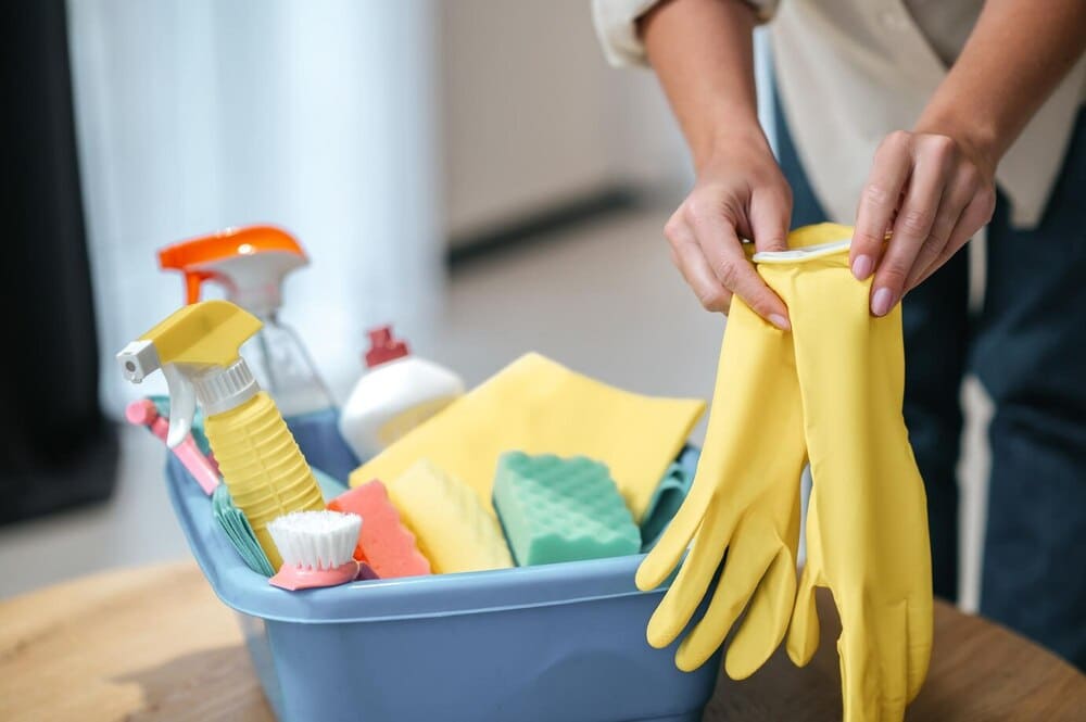 Persona preparando guantes de limpieza con suministros al frente, crucial para la limpieza de la casa después de un fallecimiento.