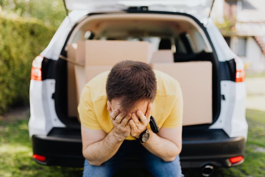 Hombre angustiado sentado en la parte trasera de un coche con cajas, reflejando la carga emocional de decidir si es malo tener pertenencias de un difunto.